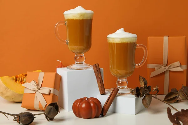 Pumpkin coffee, spices and gift boxes on orange background