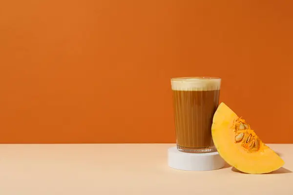 Pumpkin coffee in glass and piece of pumpkin on orange background, space for text