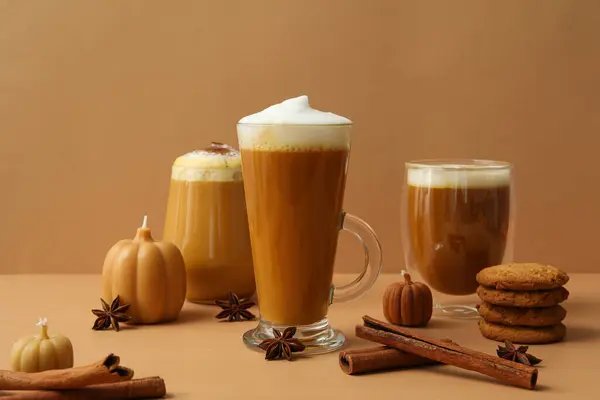 Pumpkin coffee in glasses, spices and candles on beige background