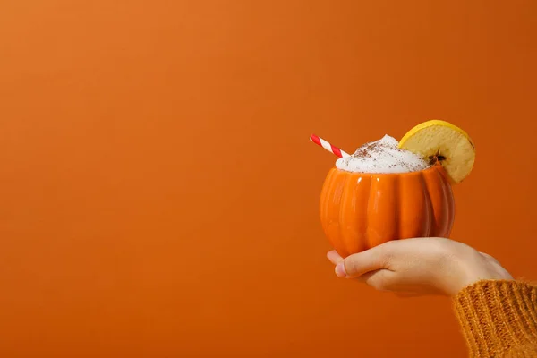 Pumpkin coffee in female hand on orange background, space for text