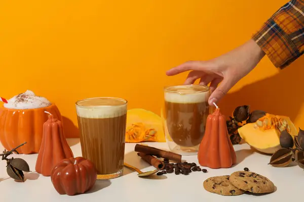 Pumpkin coffee, spices, pumpkins and hand on orange background