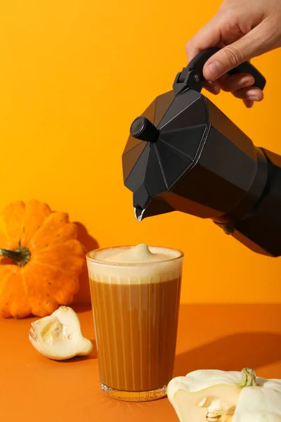 Pumpkin coffee, zucchini and coffee maker in hand on orange background
