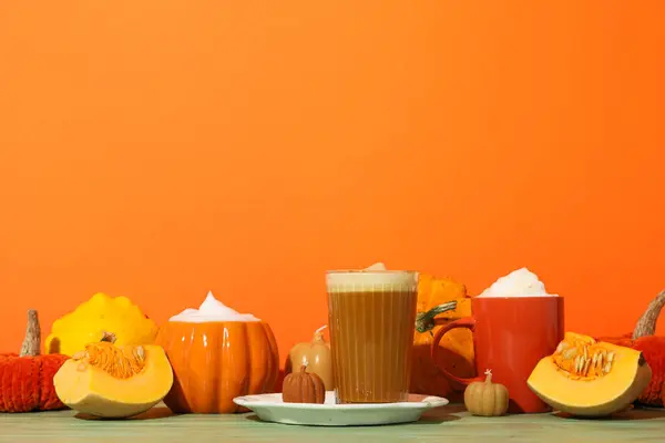 Pumpkin coffee, pumpkins and candles on orange background, space for text