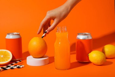 Teneke kutular, meyve suyu, limon ve turuncu arka planda el olan cam şişe.