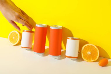 Teneke kutular, narenciye meyveleri ve sarı arka planda el.