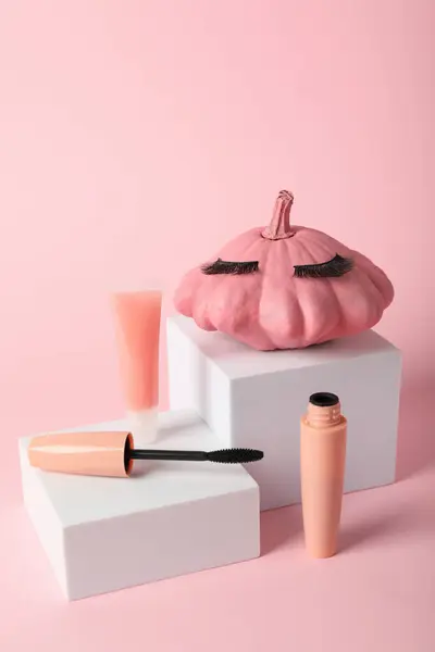 Pink pumpkin with eyelashes and cosmetics on a pink background