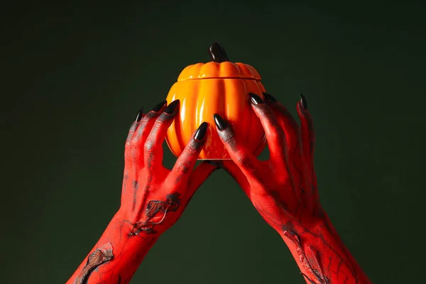 Spooky, red hands of the monster are holding a pumpkin
