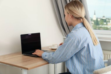 Elinde kahve olan bir kadın dizüstü bilgisayarla çalışıyor.