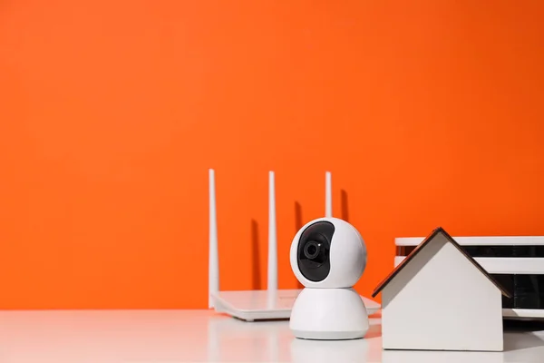 Wooden house, router, security camera and vacuum cleaner on orange background, space for text