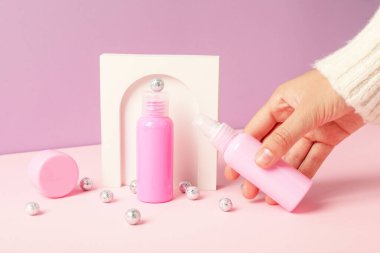 Kozmetik şişeleri, gümüş toplar, dekorasyon ve pembe arka planda el.