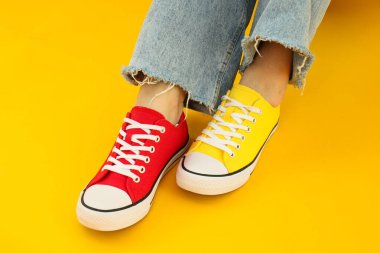 Sarı arka planda çok renkli spor ayakkabılarla bacaklar..