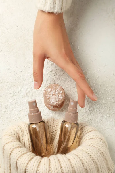 Cosmetic bottles in sweater and hand on white background, top view