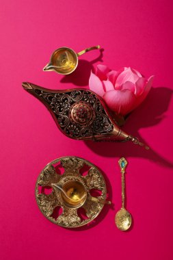 Pembe arka planda bakır çatal bıçak ve çiçek, üst manzara.