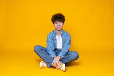 Sarı arka planda yerde oturan kıvırcık çocuk..