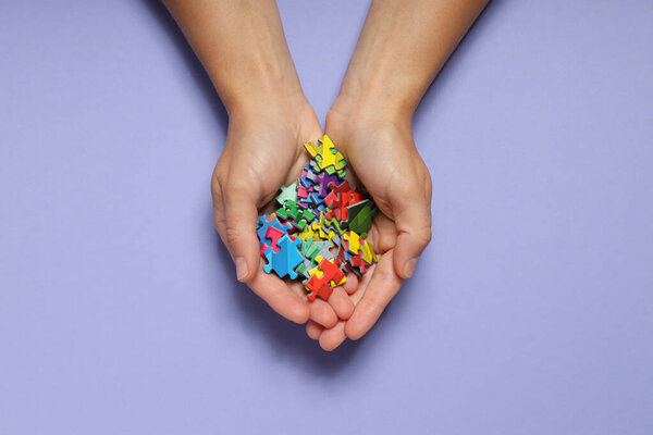 Colored puzzles in hands on purple background, top view