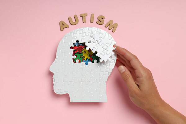 Puzzle head, word autism and hand on pink background, top view