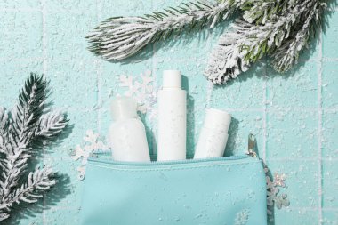 Poşette kozmetik kavanozları ve mavi arka planda köknar dalları, üst görünüm