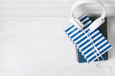 Beyaz ahşap arkaplan üzerine kitap yığını üzerindeki kulaklıklar, metin için boşluk