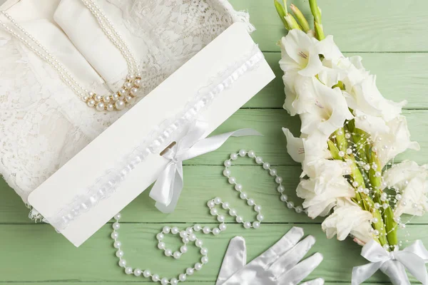 Box with wedding dress, flowers and beads on green background, top view