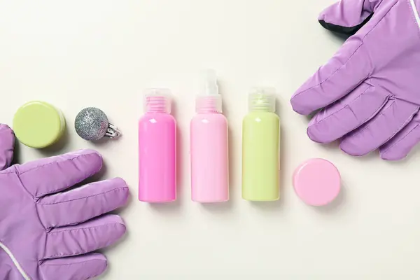 Cosmetic jars and ski gloves on white background, top view