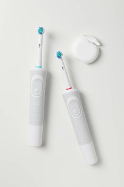 Elektrikli diş fırçaları ve beyaz arka planda diş ipi, üst görünüm