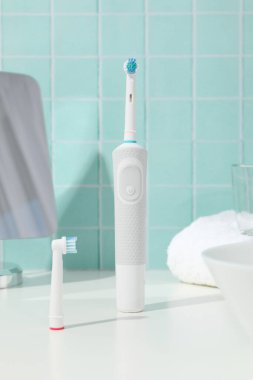 Mavi arka planda elektrikli diş fırçası, ayna, cam ve havlu.