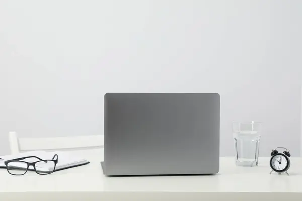 Laptop, glasses, glass and alarm clock on table on white background