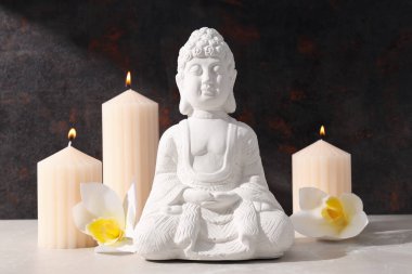 Beyaz Buda heykeli, çiçekler ve koyu arkaplanda mumlar.