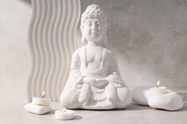 Buda 'nın beyaz heykeli, bej arkaplanda mumlar ve taşlar