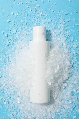 Mavi arka planda kozmetik şişesi ve kar, üst manzara