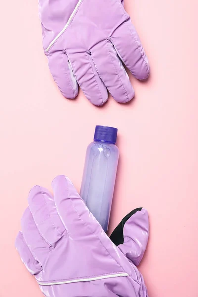 Cosmetic bottle and ski gloves on pink background, top view