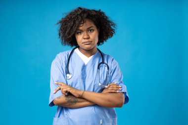 Mavi arka planda steteskobu olan üzgün kıvırcık kadın.