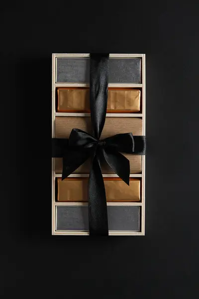 Chocolates in box with ribbon on black background, top view