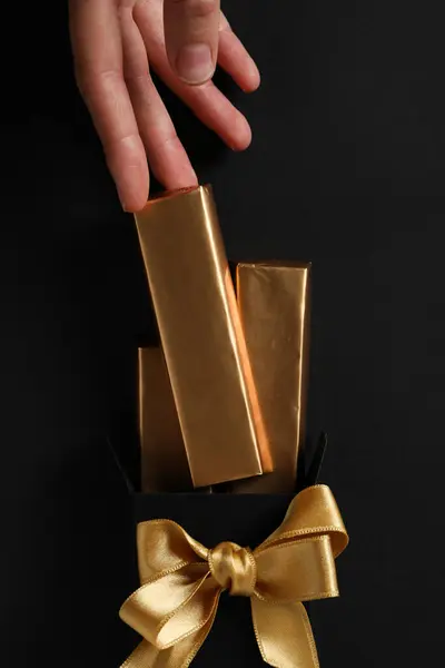 Chocolates in foil, ribbon and hand on black background, top view