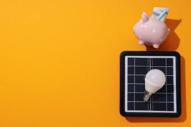 Güneş paneli, ampul ve sarı arka planda domuz kumbarası, metin için boşluk