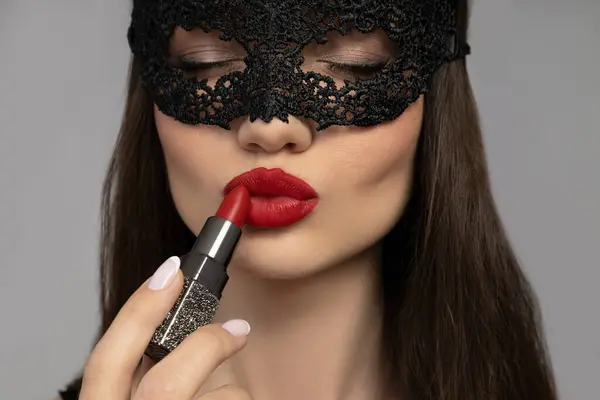 Attractive girl in a black mesh mask and lipstick in her hand