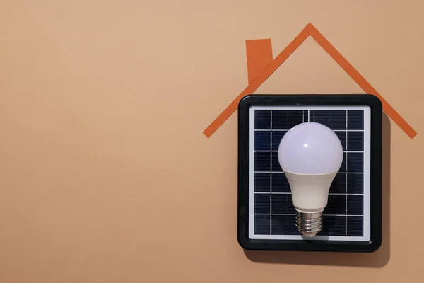 Solar panel, light bulb and paper roof on beige background, space for text