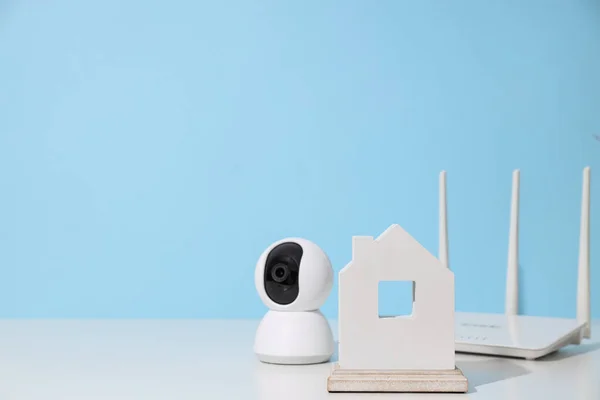 Wooden house, router and security camera on blue background, space for text