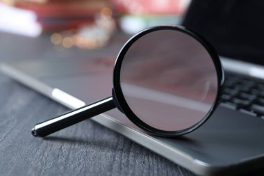 Diz üstü bilgisayarda büyüteç, ahşap arka planda klavye, kapat