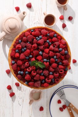 Böğürtlenli turta, fincanlar, çaydanlık ve tabaklar açık ahşap arka plan, üst manzara