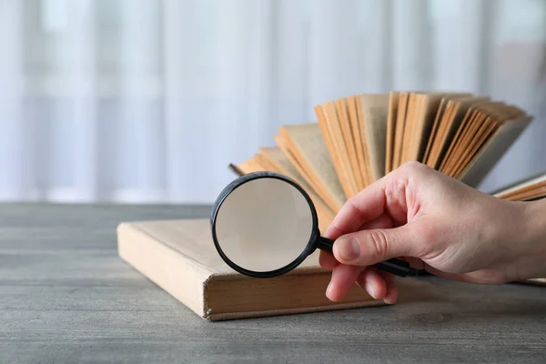 Magnifier in hand and open book on wooden table on light background