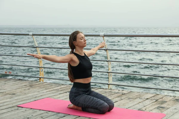 Woman on yoga mat on wooden floor at sea