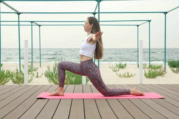 Woman on yoga mat on wooden floor outdoors