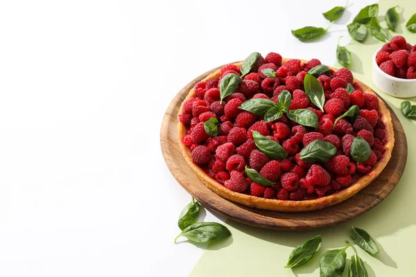 Berry pie on wooden plate and basal on light green background, space for text