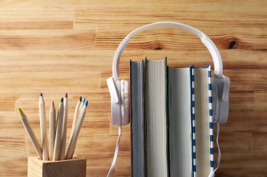 Kitaplardaki kulaklıklar ve tahta arka plandaki kalemler.