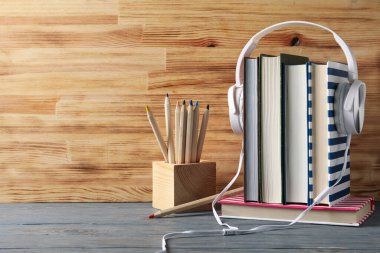 Kulaklıklı kitaplar ve tahta masadaki kalemler. Okula geri dön.