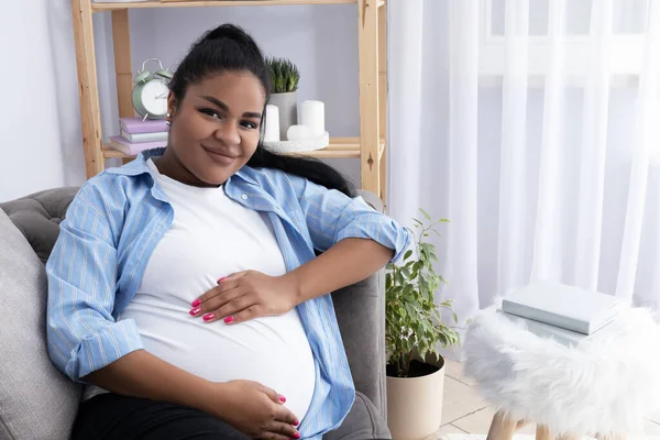 Pregnant African American woman in room on couch.