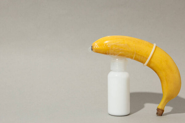 Lubricant with a banana in a condom, on a gray background.