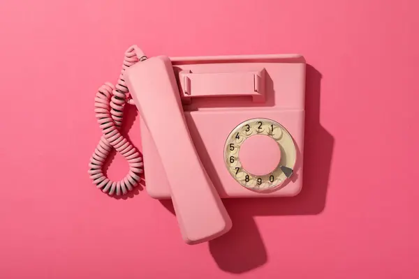 Pink landline phone on pink background, top view