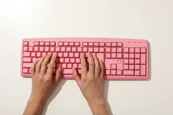 Pink computer keyboard and hands on white background, top view